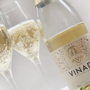 Vinada Airen Gold non alcoholic sparkling bottle on bench with two glasses with sparkling in it