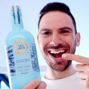 Man holding non-alcoholic gin made by sea arch and smiling