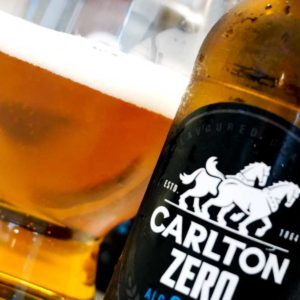 Carlton Zero Non Alcoholic Beer in glass next to bottle close up